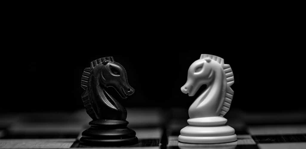 A black and a white chess knight facing each other on a chessboard